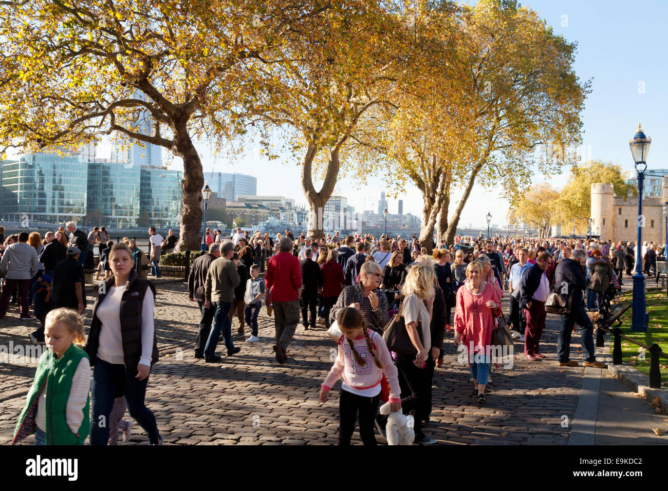 Crowds of people walking alongside the river Thames at the Tower of London on  a sunny autumn day; London UK Stock Photo