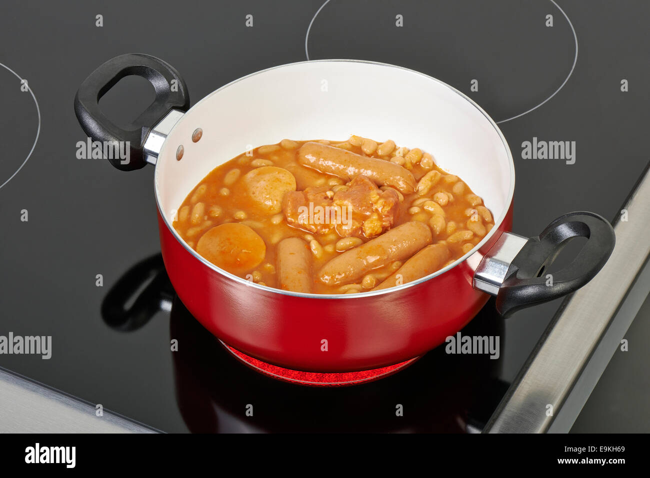 Preparing cassoulet in red ceramic pan without cover on Electric hob in modern and domestic kitchen Stock Photo
