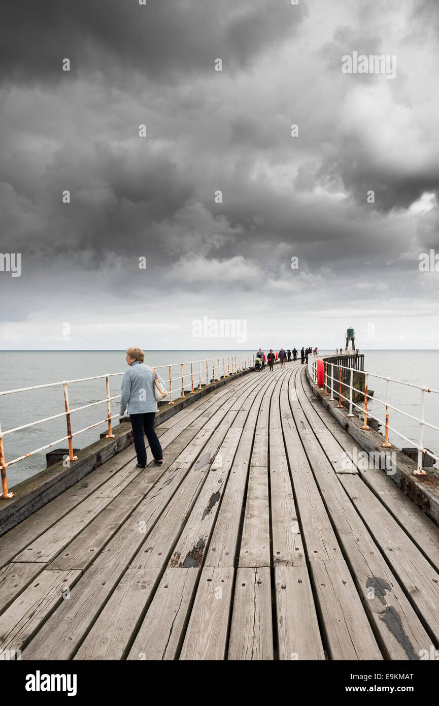 A stormy sky over Whitby Pier as tourists walk along the wooden planks. Stock Photo