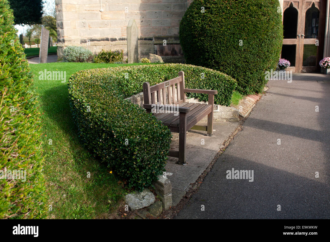 A bench in and clipped hedge in All Saints churchyard, Kings Bromley, Staffordshire, England, UK Stock Photo