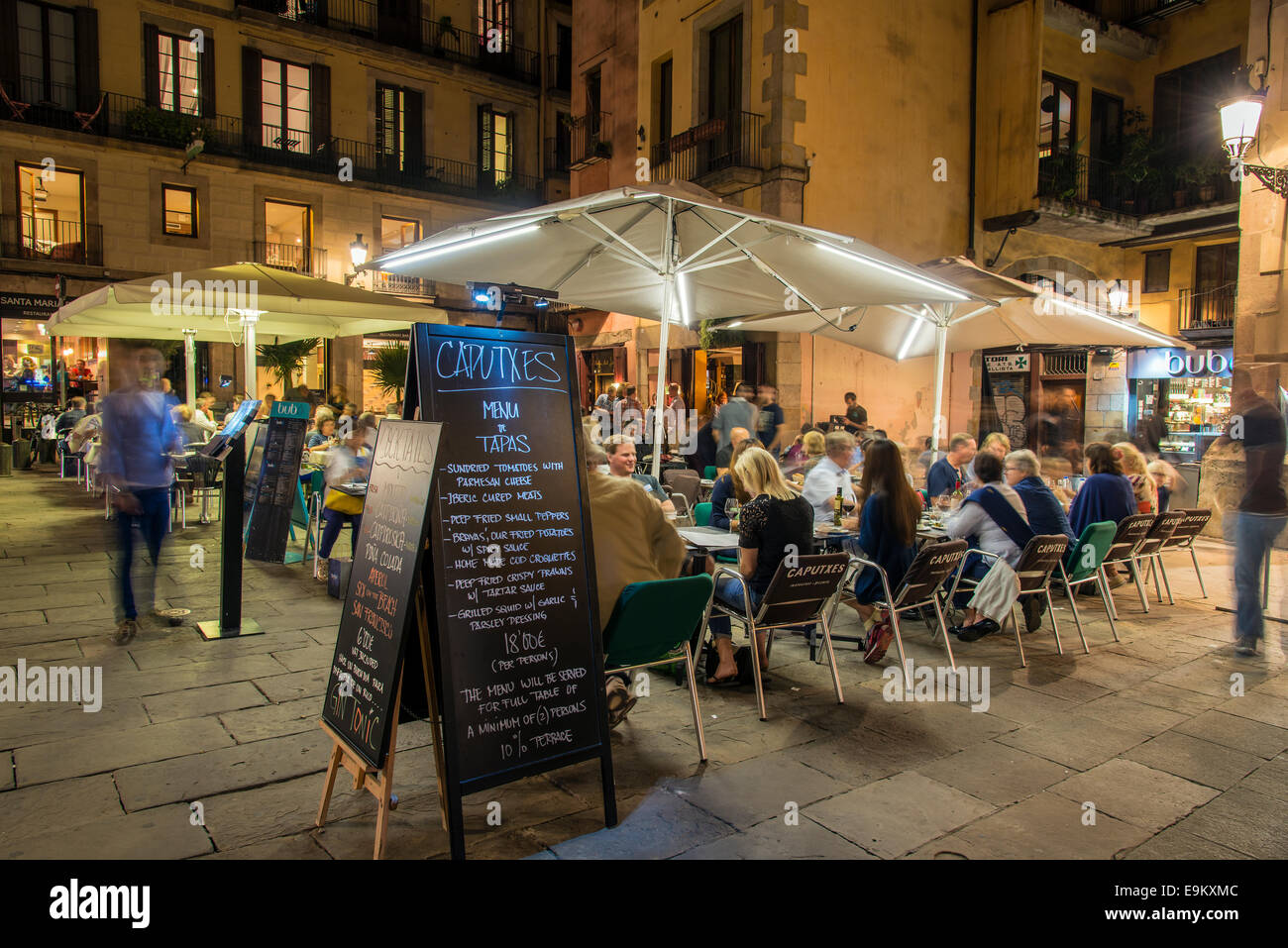 Night view of an outdoor cafe serving tapas with menu blackboard and people seated at tables, Barcelona, Catalonia, Spain Stock Photo