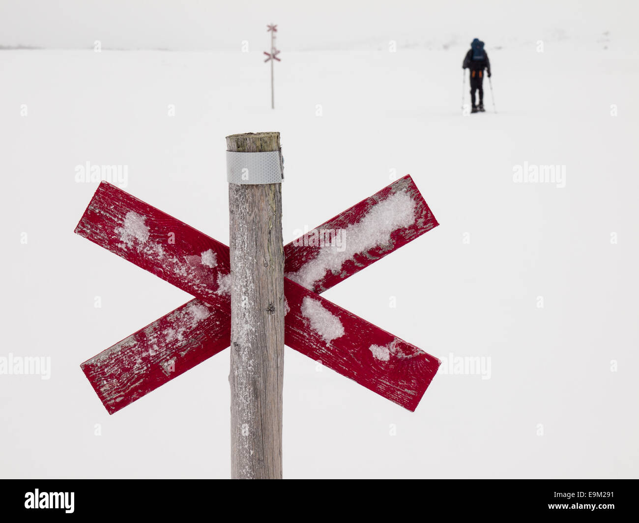 wooden trail marker next to ski trail in Northern Swedish mountain area of Sylarna (sylan) with  snowshoer out of focus behind Stock Photo