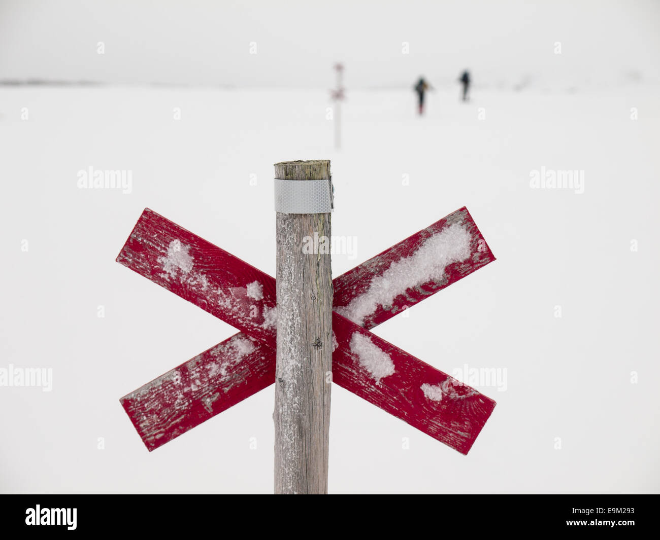 wooden trail marker next to d trail in the Northern Swedish mountain area of Sylarna (sylan) with  skiers out of focus behind Stock Photo