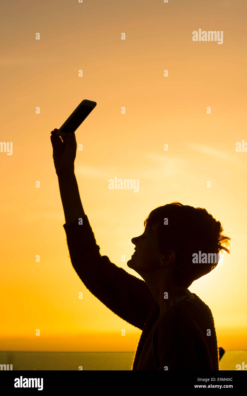 A woman uses a mobile phone on a foreign roaming network  while on holiday during sunset sunrise. Stock Photo
