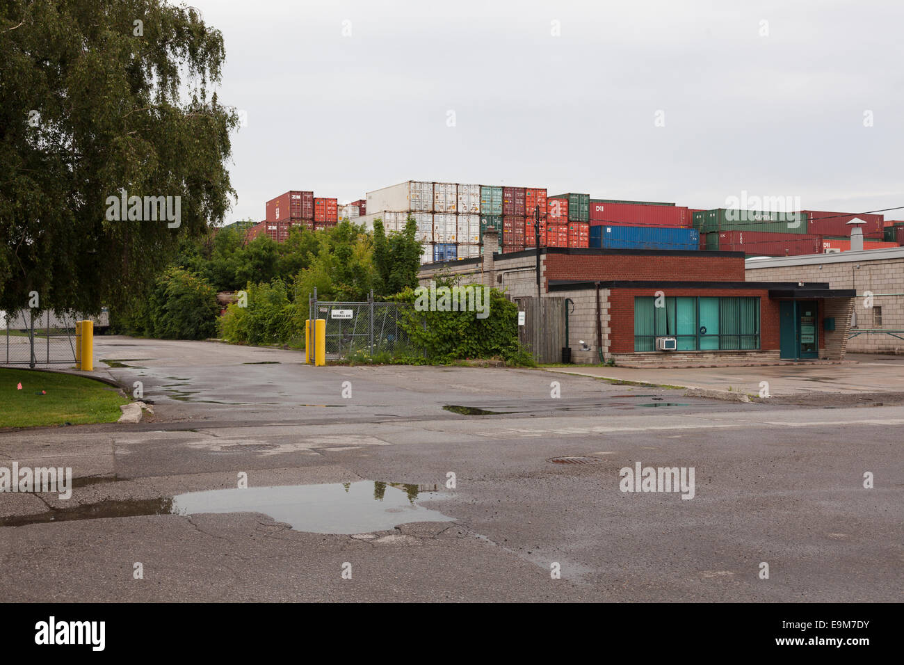 A small industrial building with stacks of shipping containers in the background. Toronto, Ontario, Canada. Stock Photo