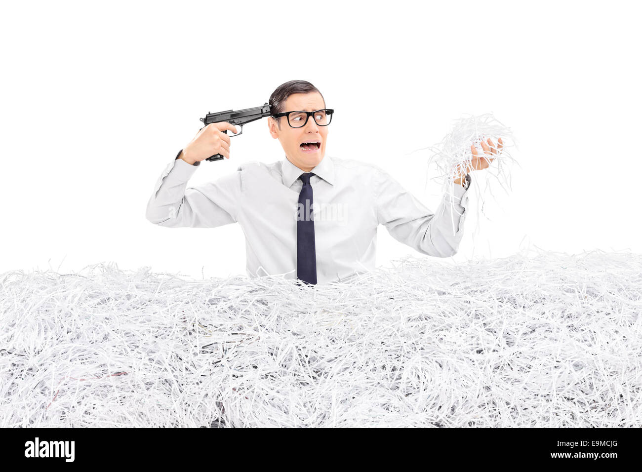 Desperate man holding a gun to his head and standing in a pile of shredded paper isolated on white background Stock Photo