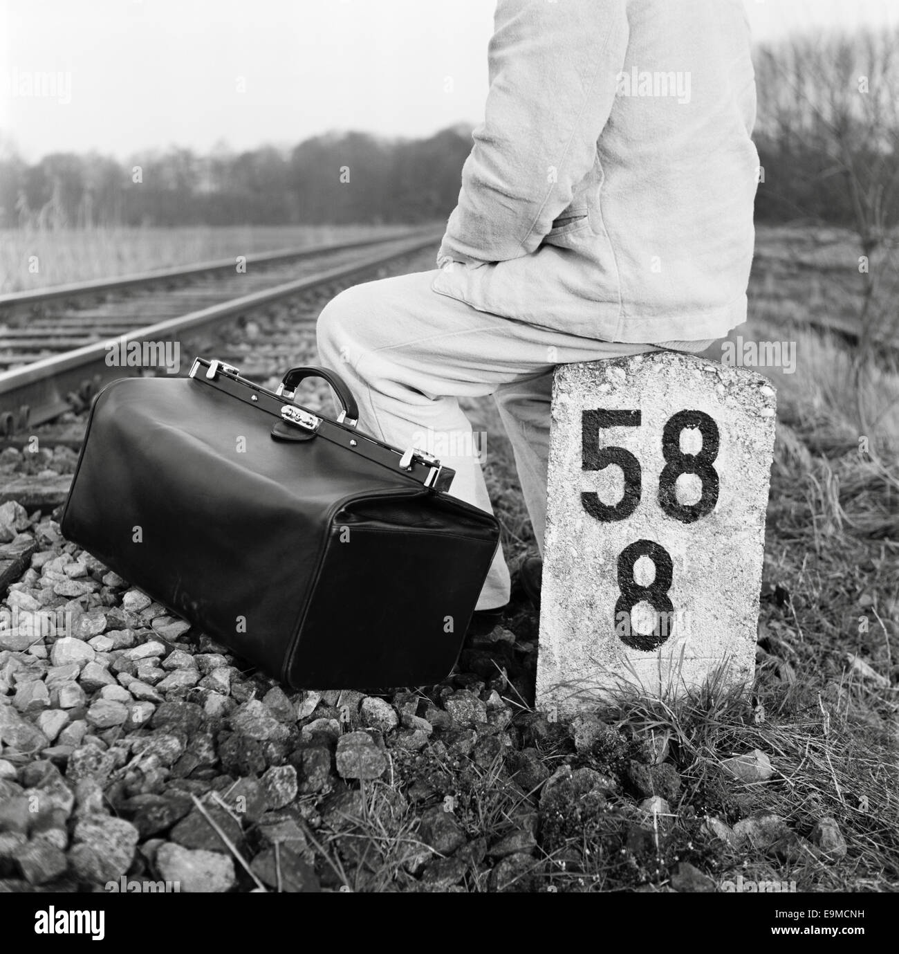 A person with a bag sitting next to train tracks Stock Photo Alamy