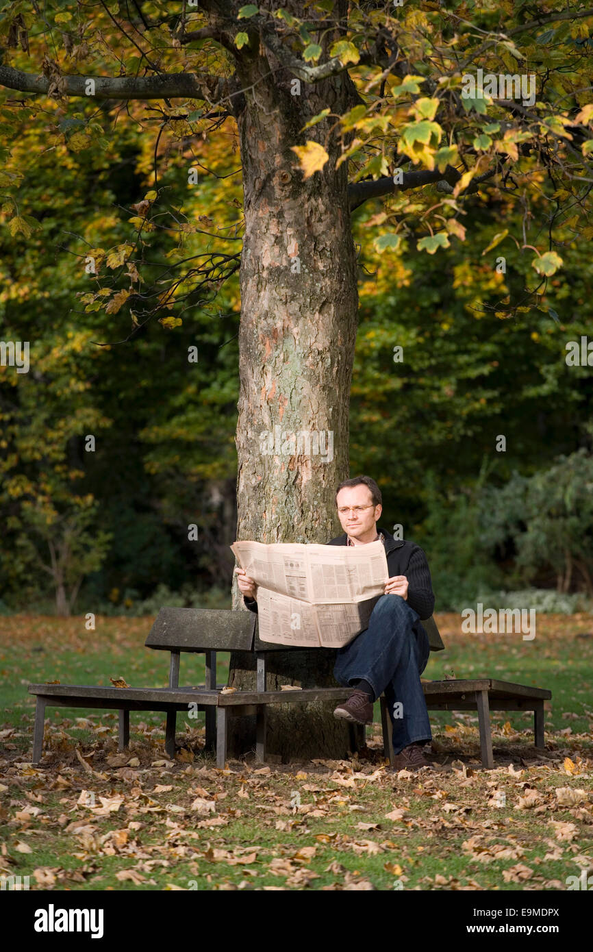 Mature man sitting on park bench reading a newspaper Stock Photo - Alamy