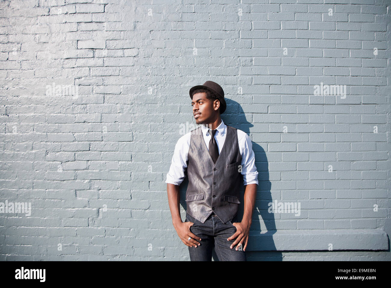 A young black man leaning against a brick wall Stock Photo - Alamy