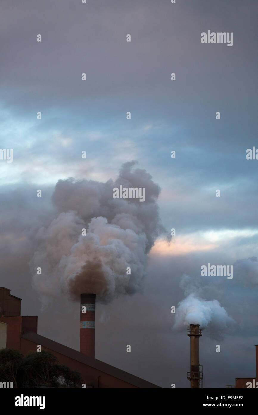 Smoke emitting from chimneys against cloudy sky Stock Photo