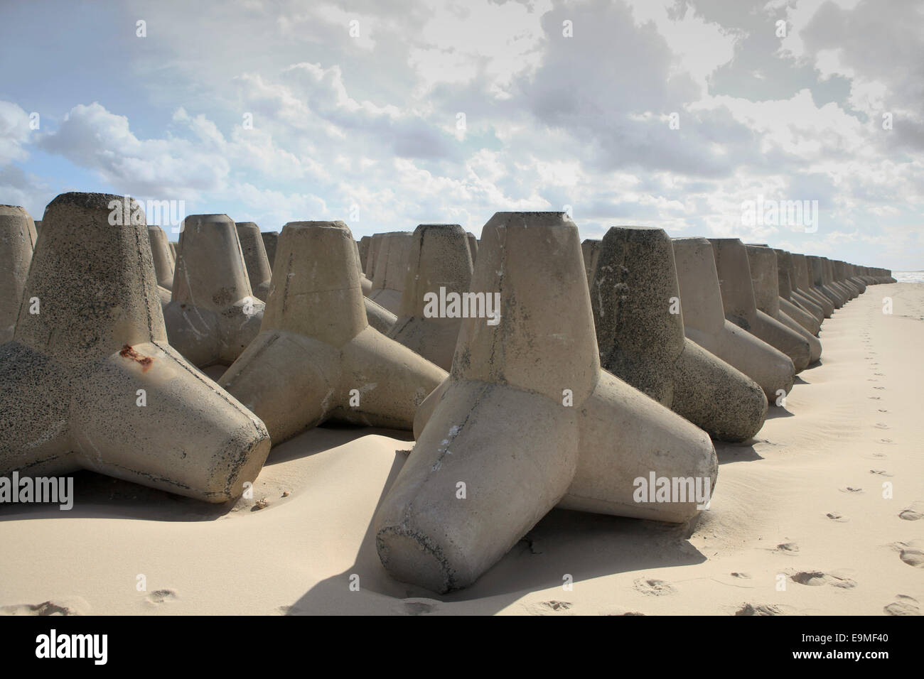 Tetrapod rocks arranged on sandy beach against cloudy sky Stock Photo