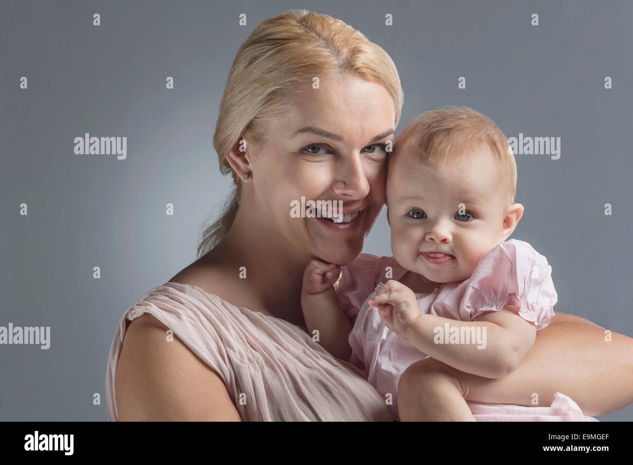Portrait of happy mother carrying cute baby girl against gray background Stock Photo