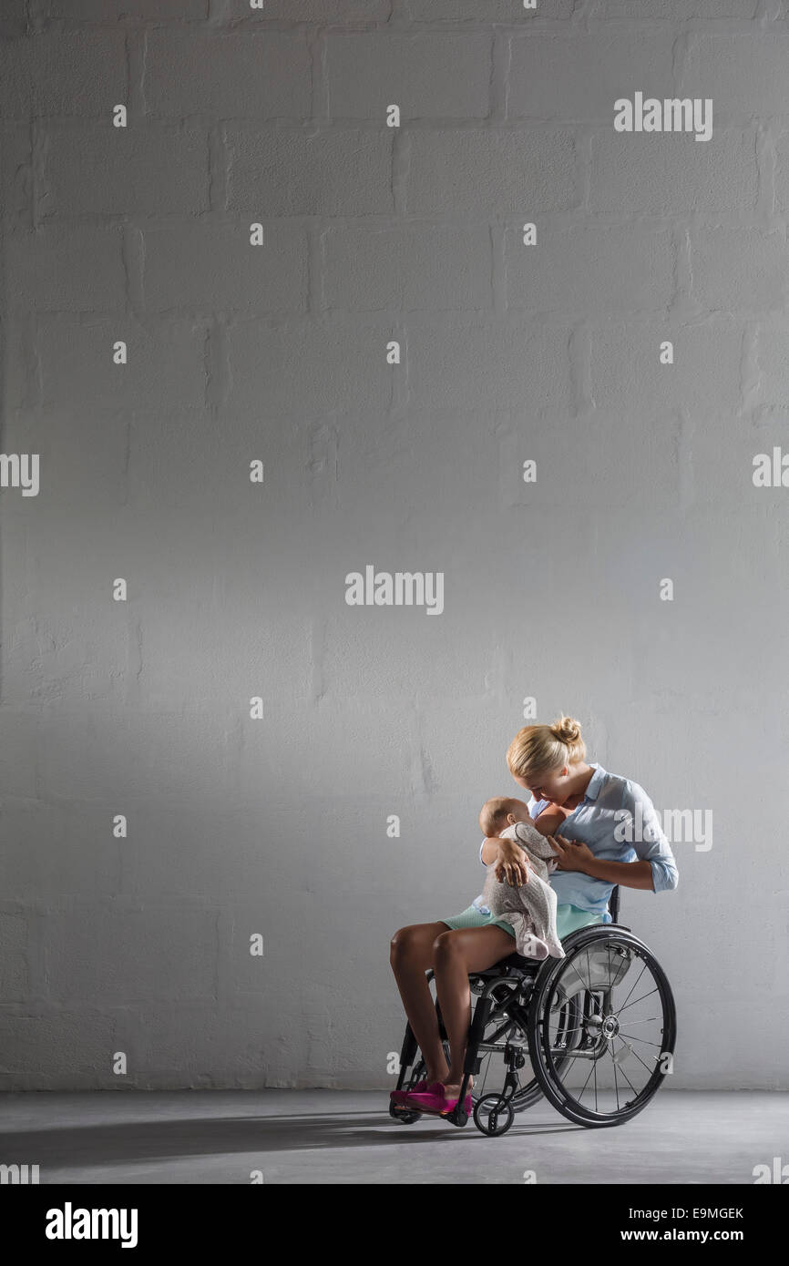 Full length of woman breastfeeding baby girl in wheelchair against gray wall Stock Photo Alamy