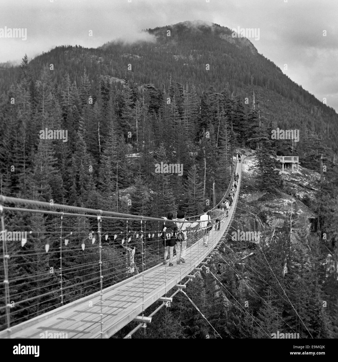 People walking on footbridge leading towards mountain Stock Photo