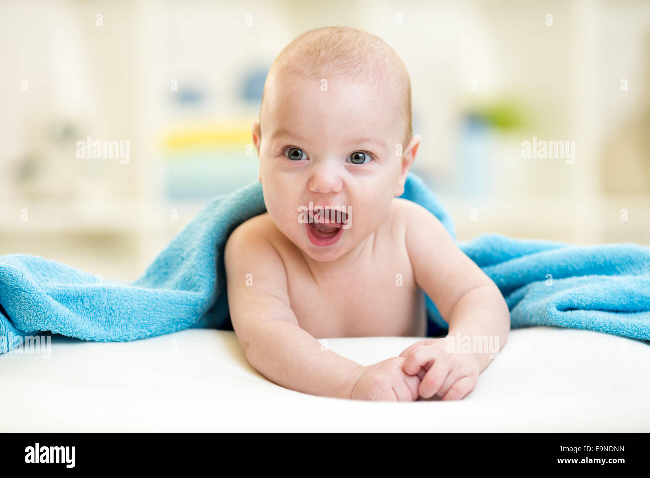 Cheerful baby boy looking out under a blue towel after bathing Stock
