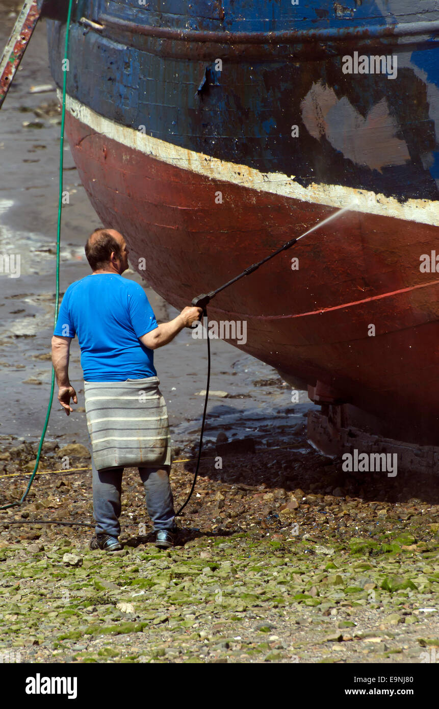Man pressurewashing the hull of a fishing boat in Port Seton Harbour
