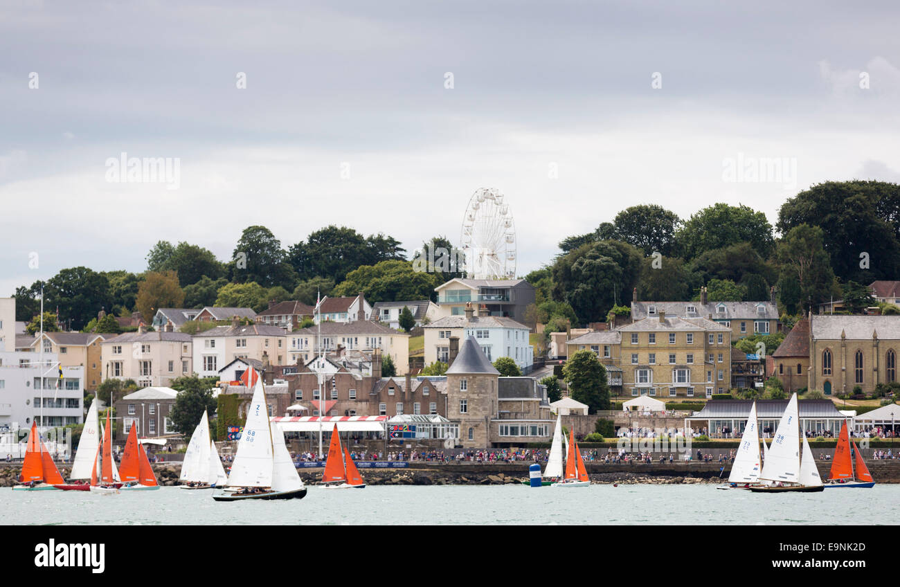 The Squibs (red sails) and Victory class yachts pass the Royal Yacht Squadron during Aberdeen Asset Management Cowes Week. The e Stock Photo