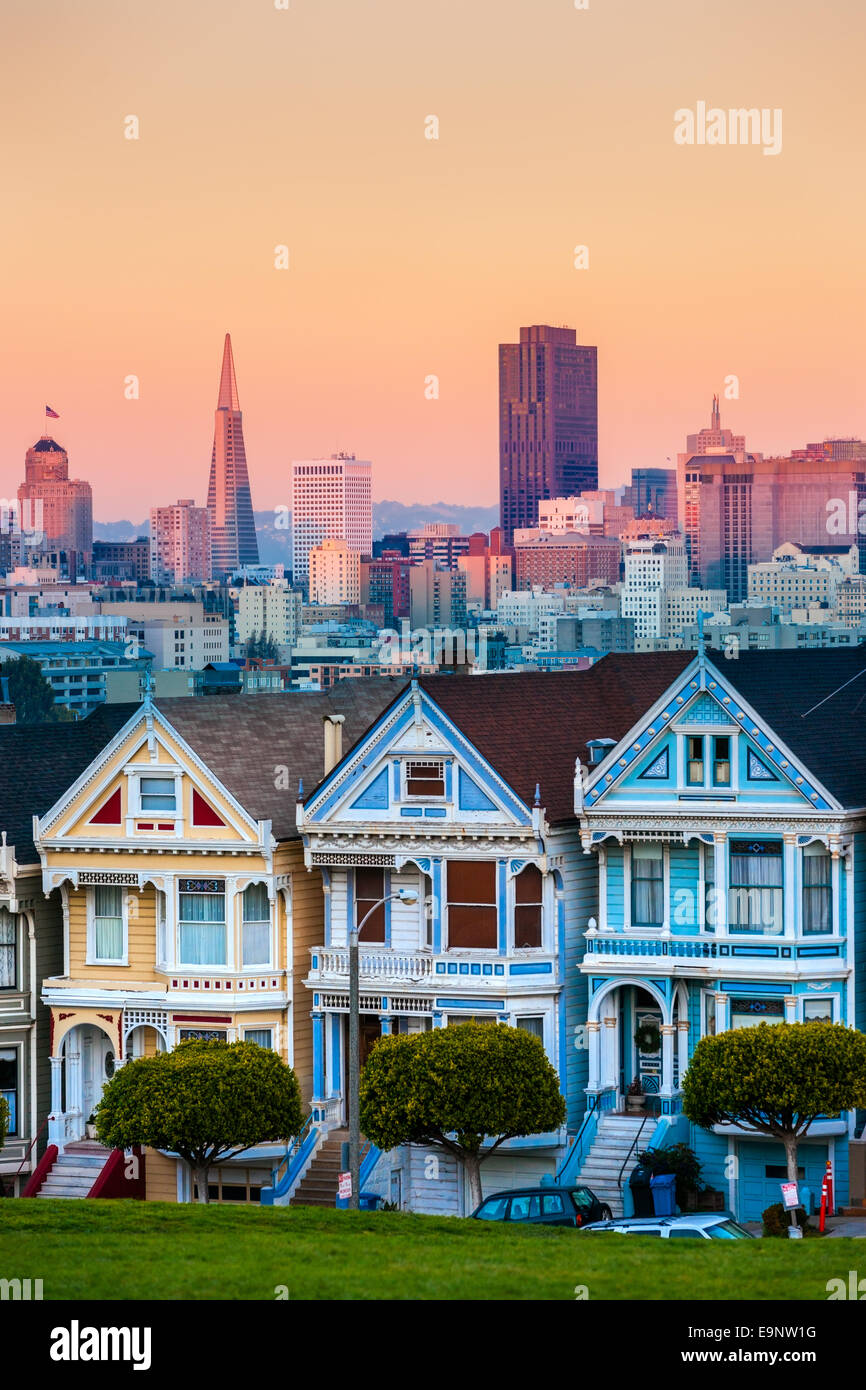 The Painted Ladies of San Francisco, California sit glowing amid the backdrop of a sunset and skyscrapers. Stock Photo