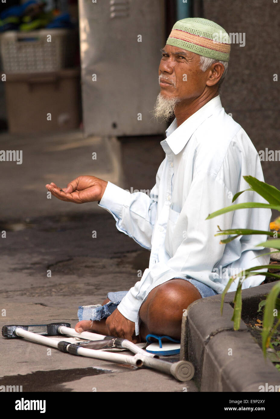 Man with one leg begging in the street. There are many beggars in and around central Bangkok Stock Photo