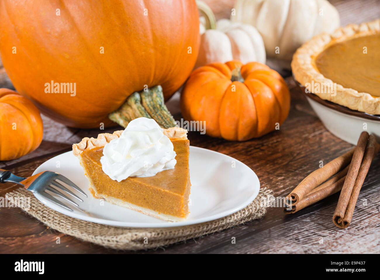 Slice of a pumpkin pie and pumpkins on wooden table Stock Photo