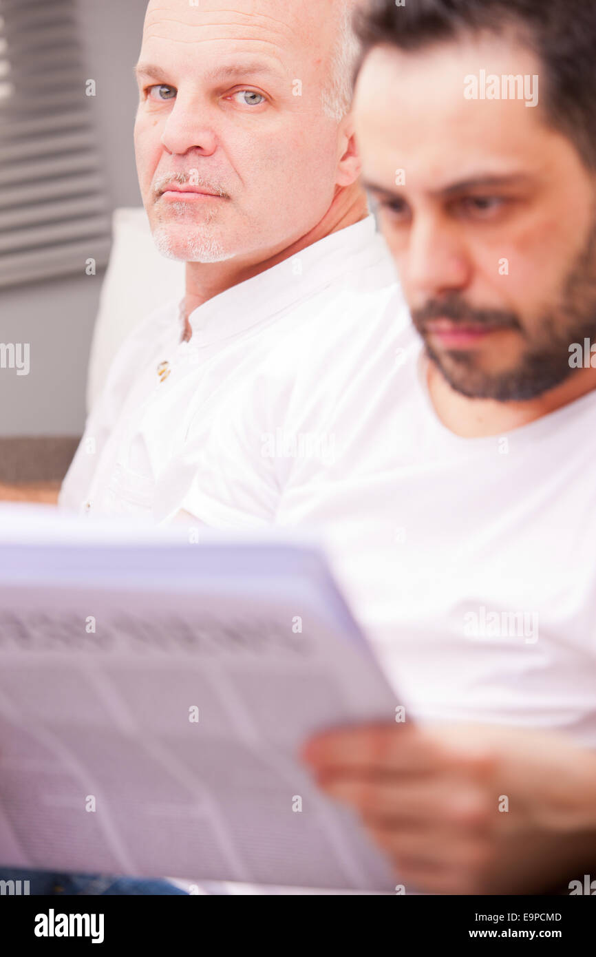 serious man with a friend reading newspaper in a living room Stock