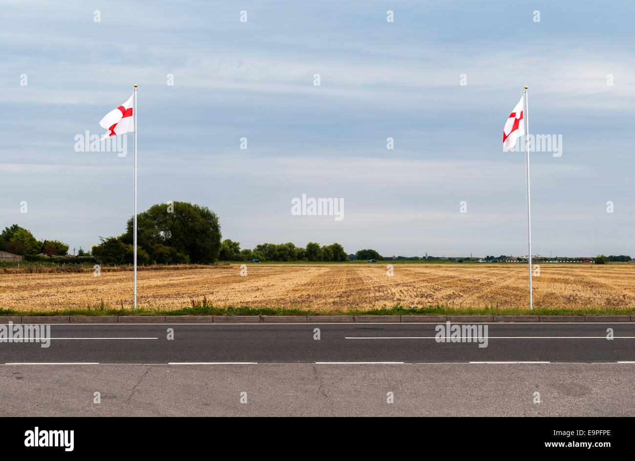 Two flagpoles flying the St George's Cross stand by the roadside in Romney Marsh, Kent, UK Stock Photo