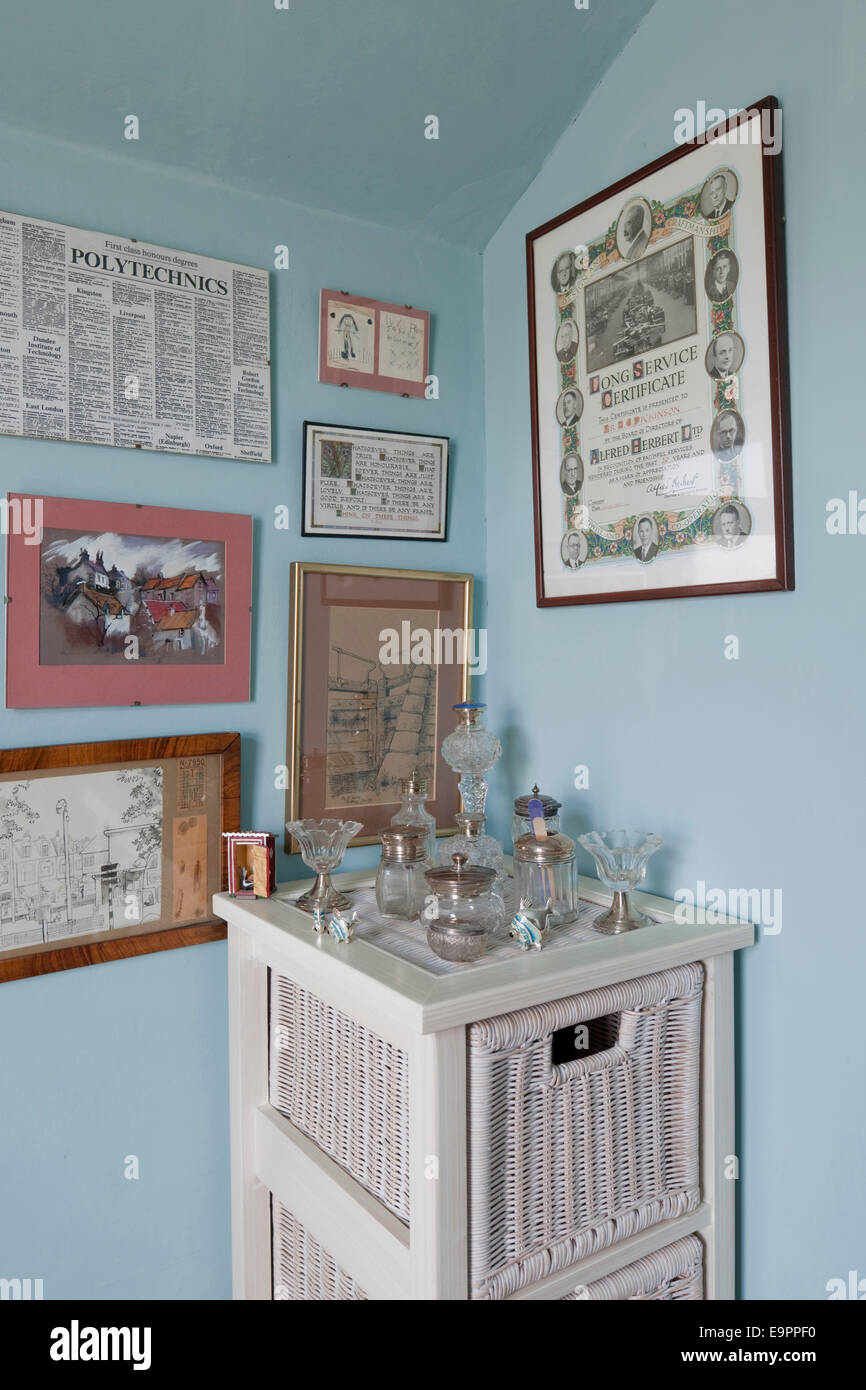 Painted wicker storage with display of old glass bottles and framed illustrations in UK home. Stock Photo