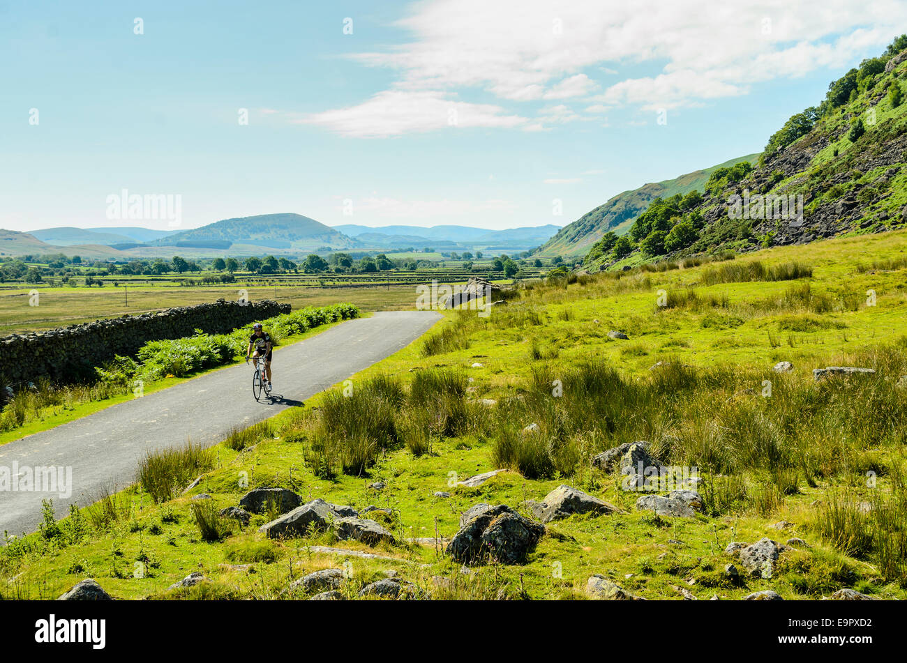 Cyclist on empty road below Carrock Fell in the northern fells of the English Lake District Stock Photo
