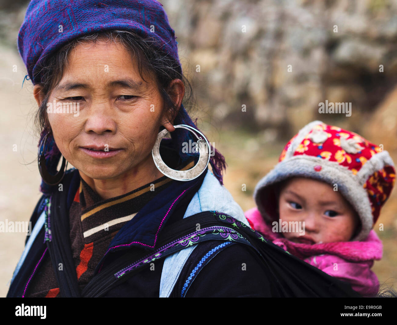 Hmong woman wearing traditional attire and jewelry and carrying an unidentified infant child in Sapa Town, North Vietnam. Stock Photo