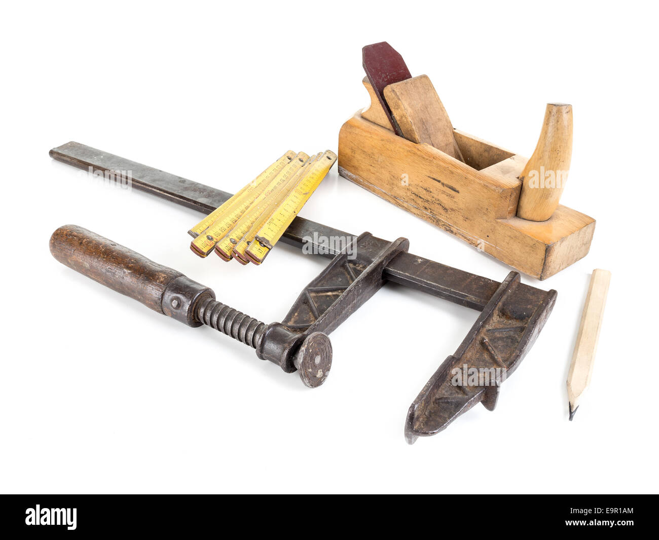 Basic set of carpenter's tools consisting of metal clamp, wooden folding ruler, plane and pencil all shot on white Stock Photo