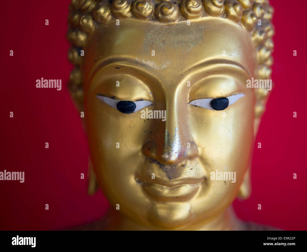 Head of old Buddha statue over vibrant red background. Stock Photo