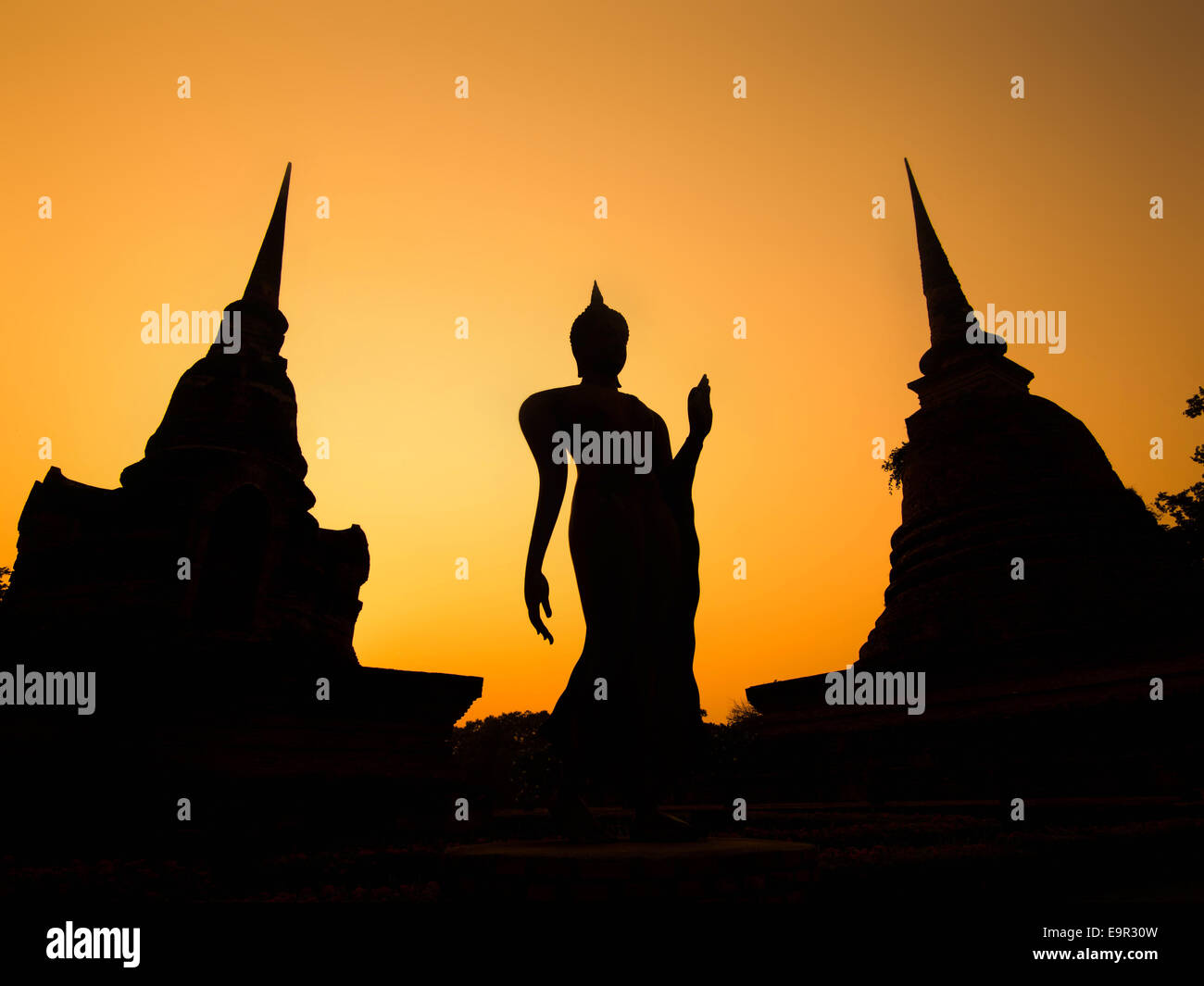 Silhouette of ancient Buddha statue and pagodas against sunset sky at Sukhothai Historical Park, Thailand. Stock Photo