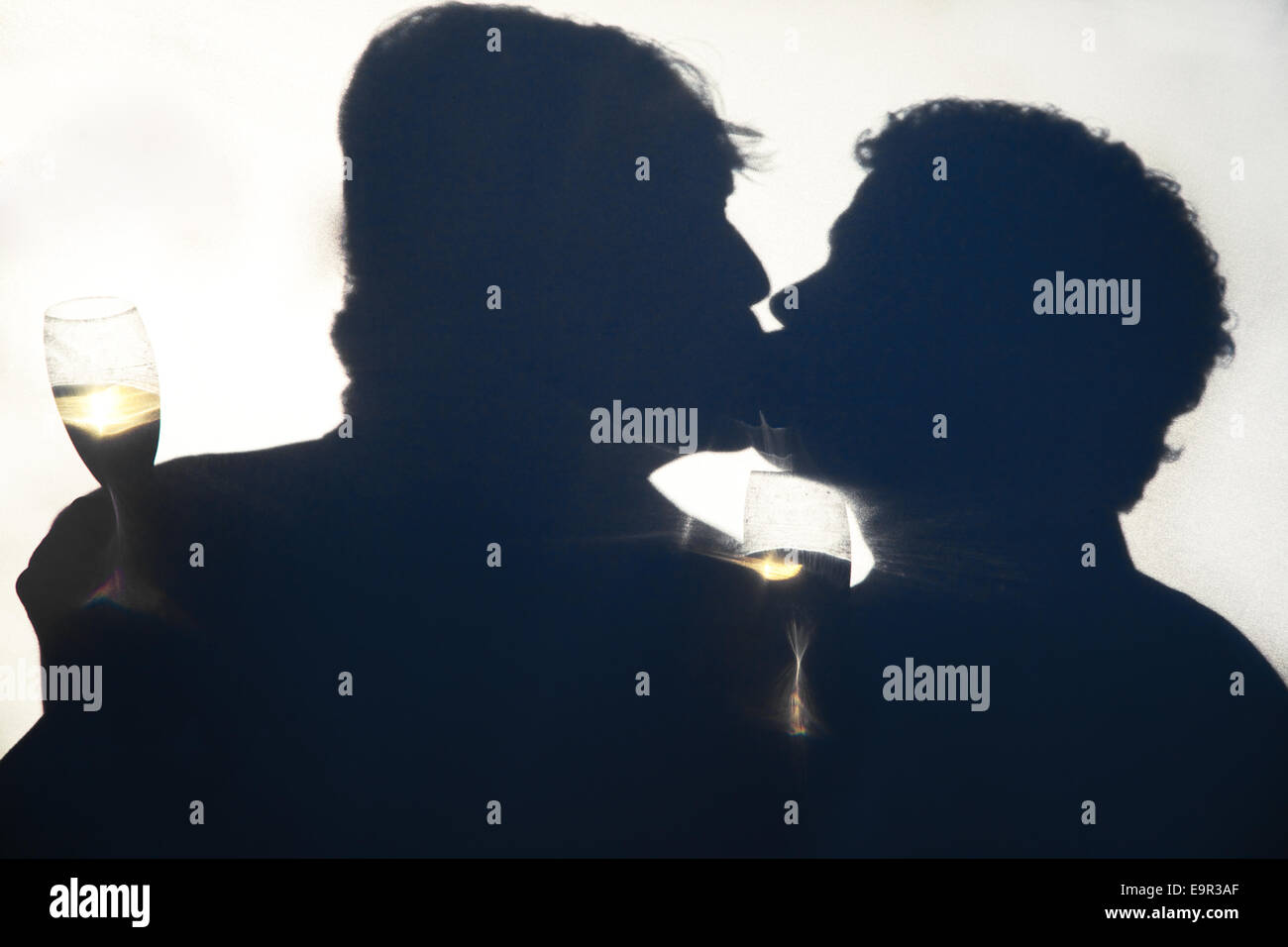 Silhouette of gay men kissing on their wedding day, holding champagne glasses behind an opaque screen. Stock Photo
