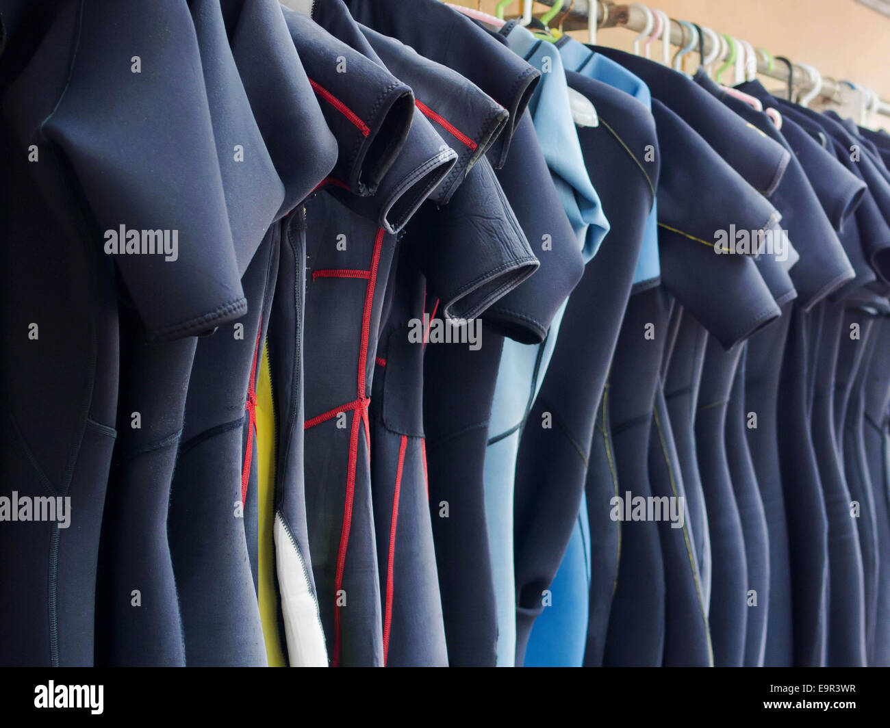 Line of multiple hanging wetsuits at scuba diving center. Stock Photo