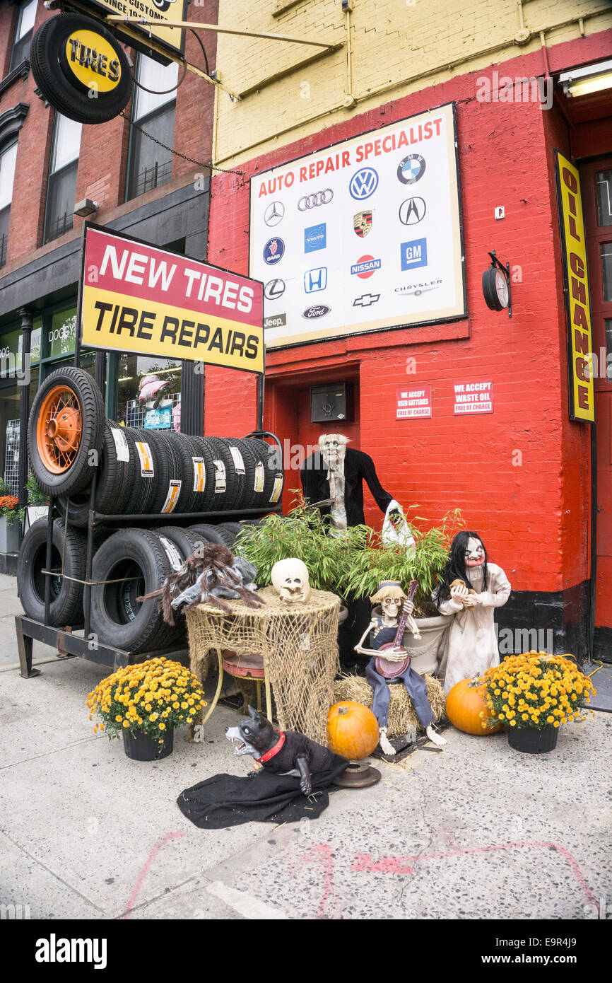 New York, USA. 31st October, 2014.  mechanized Halloween ghouls pumpkins & pots of yellow chrysanthemums join rack of new tires tyres on sidewalk outside local auto repair shop on morning of All Hallows eve Credit:  Dorothy Alexander/Alamy Live News Stock Photo