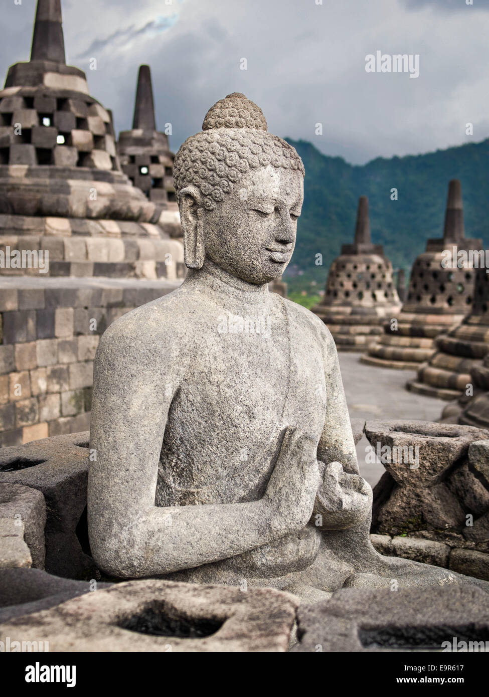 An ancient Buddha statue surrounded by stupas at Borobudur, the world's largest Buddhist monument, Java, Indonesia. Stock Photo