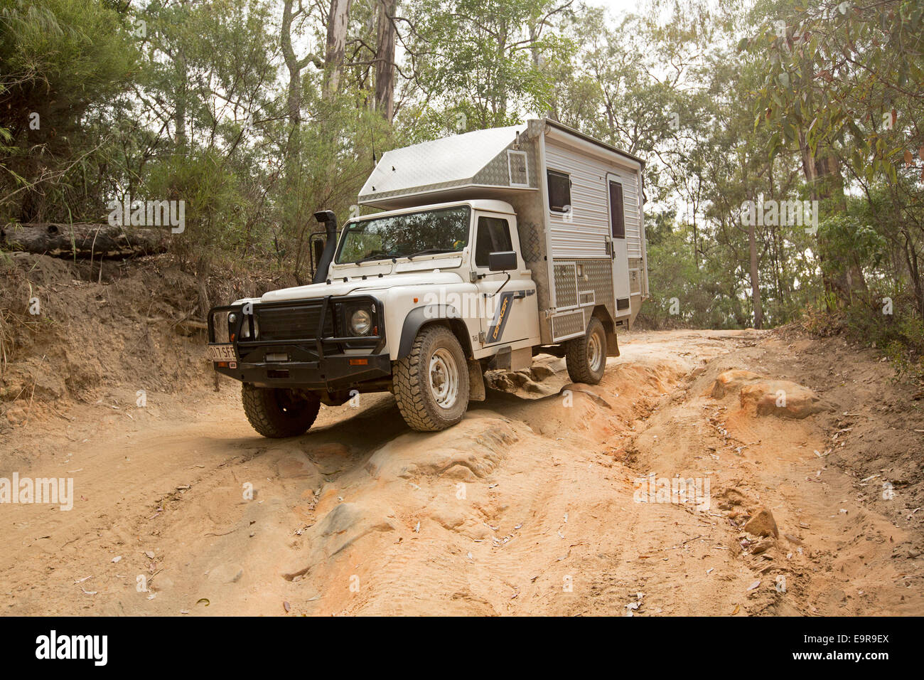Unique Land Rover campervan being driven on rough / eroded section of dirt track  through forest in Australian national park Stock Photo