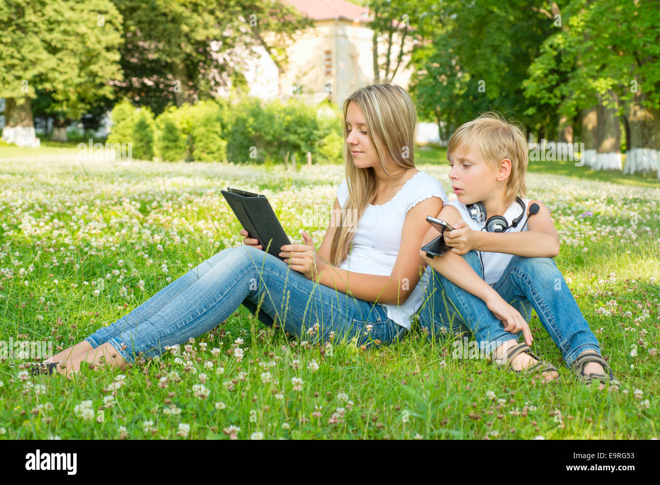 Boy and girl sitting in the park and enjoy the tablet Stock Photo - Alamy
