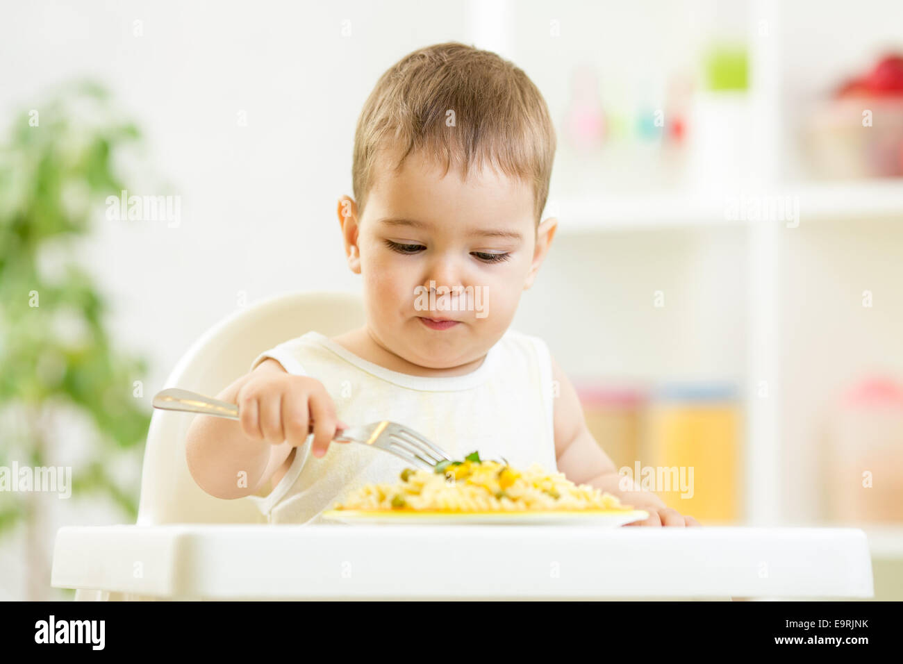one year old child boy in a highchair for feeding with a fork an Stock Photo