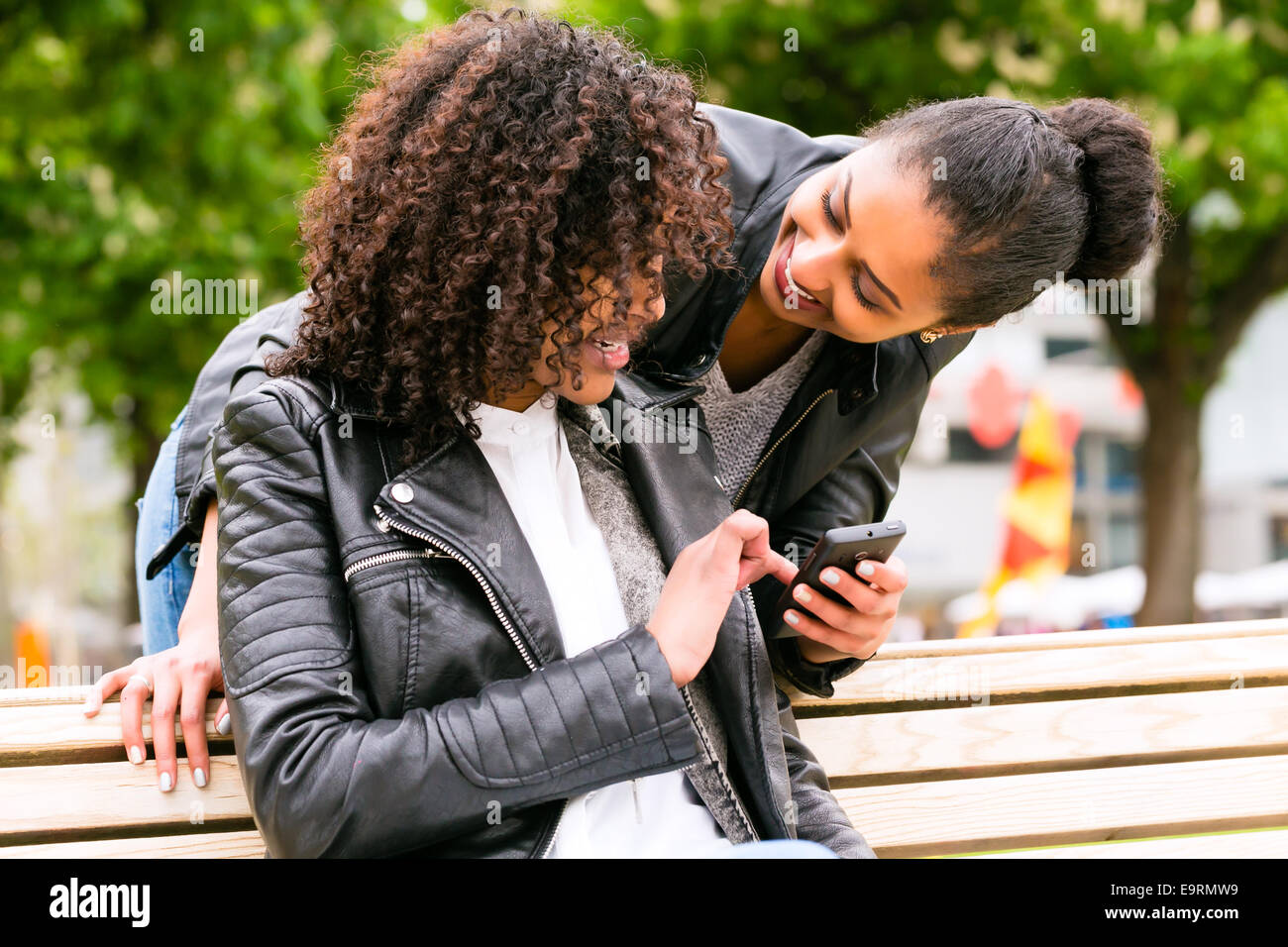 Two north African teen friends reading and writing text message on mobile phone in park Stock Photo