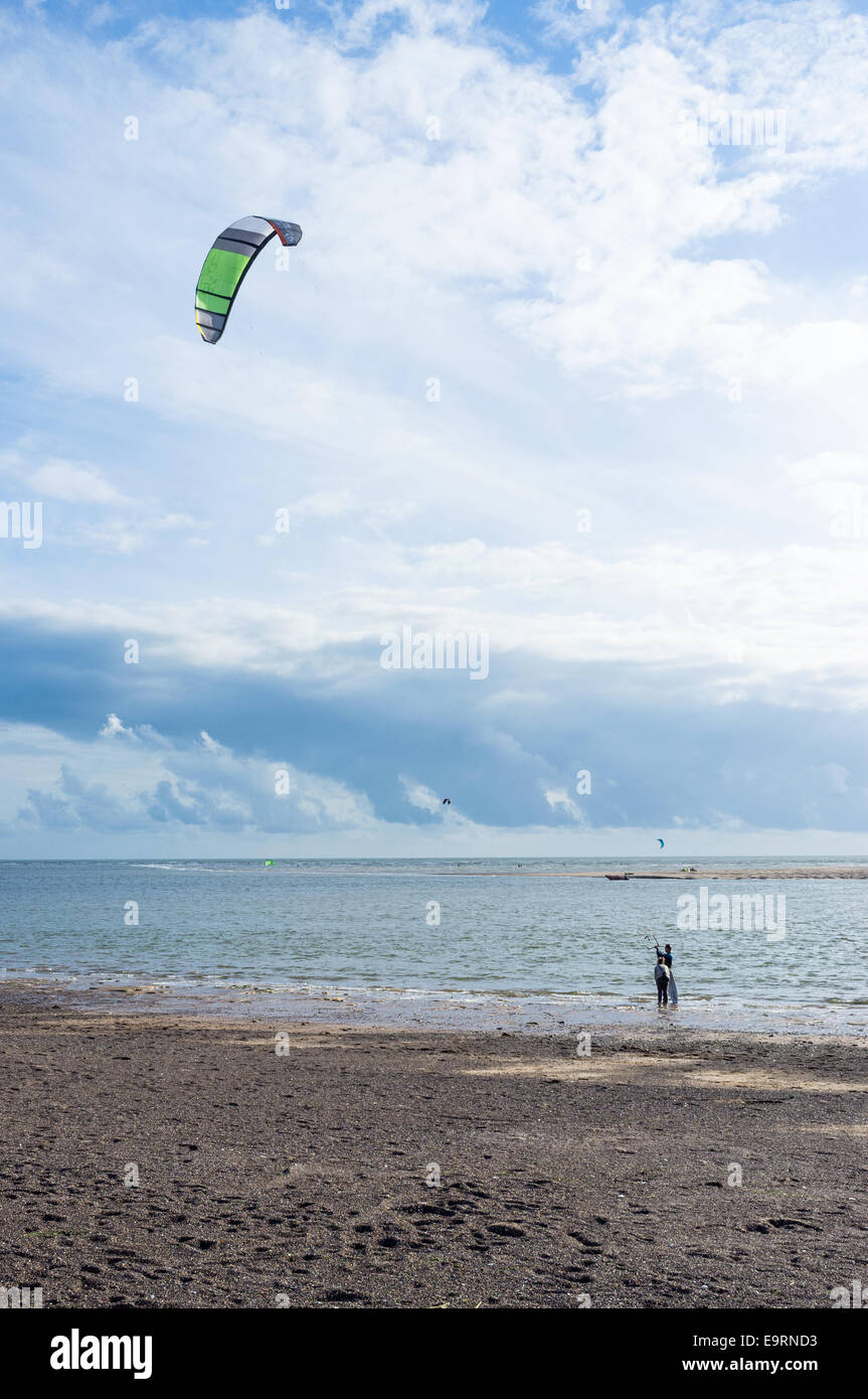 A kite surfer on a windy day at Exmouth in Devon, UK. Good conditions for kite surfing. A female companion waits on the shore. Stock Photo