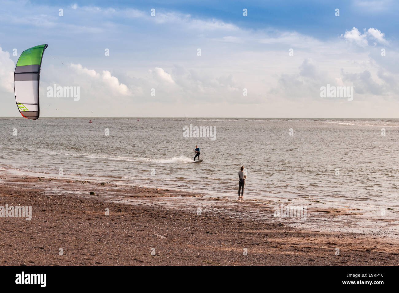 A kite surfer on a windy day at Exmouth in Devon, UK. Good conditions for kite surfing. A female companion waits on the shore. Stock Photo
