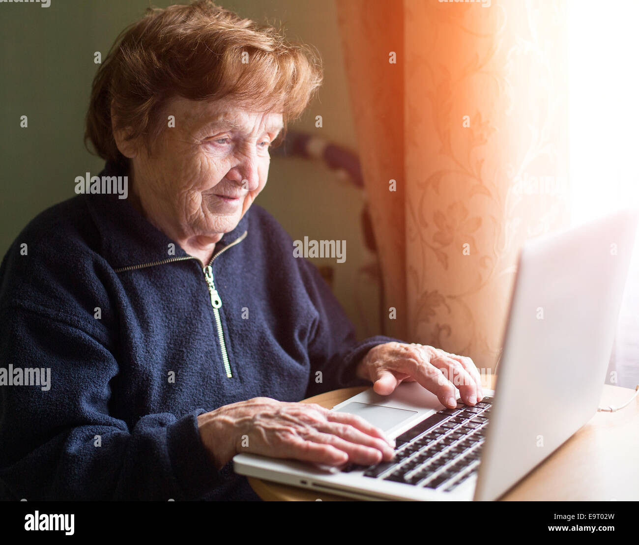 Grandmother near the window works with a laptop. Stock Photo