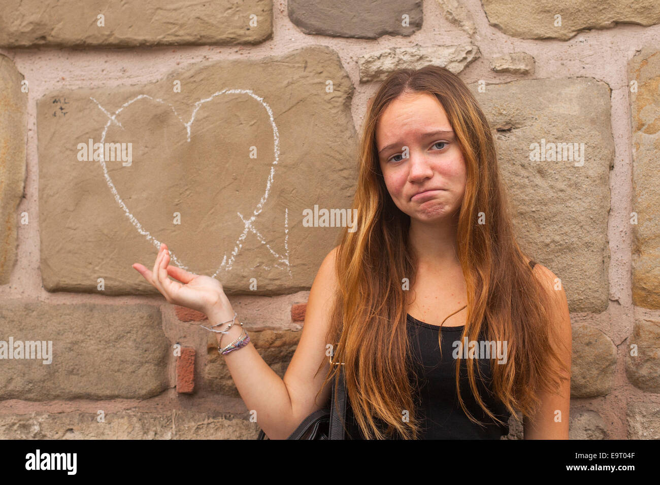Sad young pretty girl and heart in chalk on the wall. Broken love concept. Stock Photo