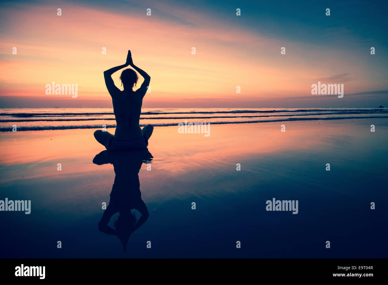 Silhouette young woman practicing yoga on beach at surrealistic sunset. Stock Photo