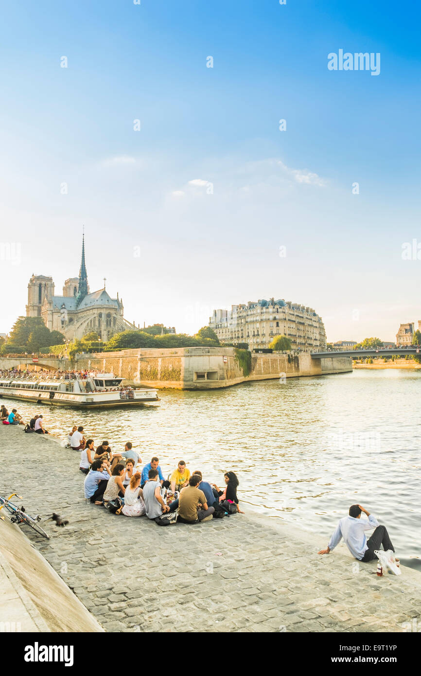 young people are having a picnic in the early evening on the banks of river seine, in the background ile de la cité Stock Photo
