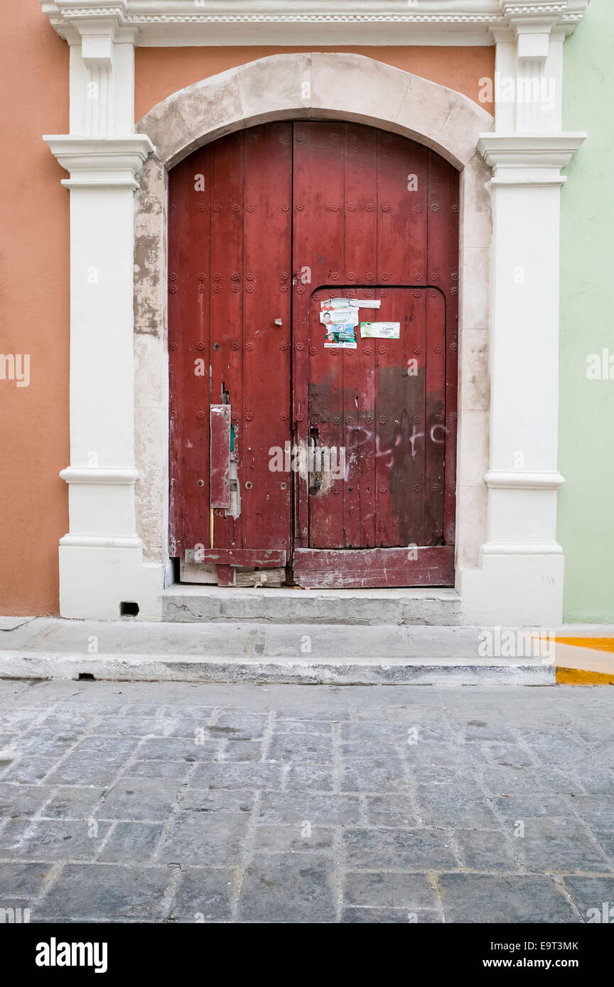 Close-up of large arched red wooden door with a smaller door cut into it on an orange Spanish colonial house, Campeche, Mexico Stock Photo