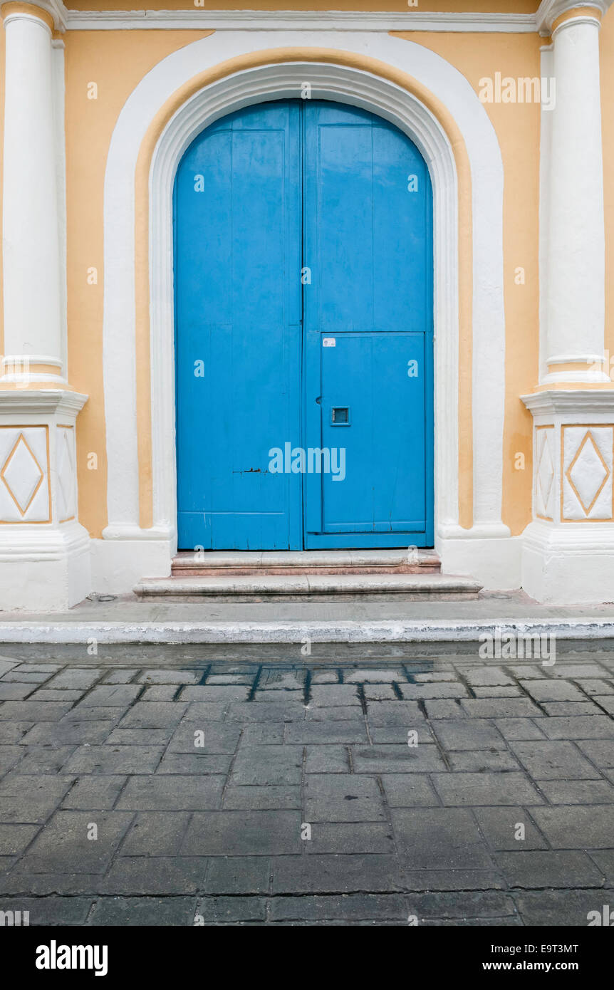 Large arched bright blue wooden doors with a smaller door cut into the right door set between decorative columns on yellow stucco house. Stock Photo