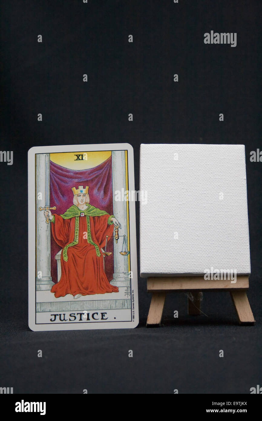 The Justice tarot card next to a blank canvas against a dark background. Stock Photo
