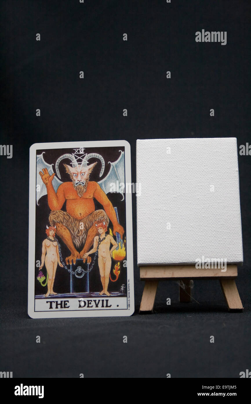 The Devil tarot card next to a blank canvas on a dark background. Stock Photo